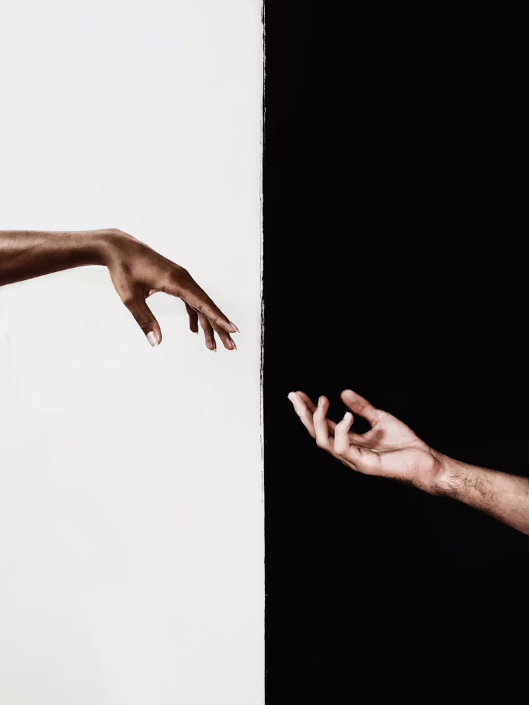 Two hands reaching across a stark black and white divide, symbolizing connection and unity.